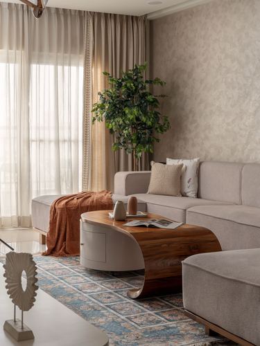 Neutral living room with curved wood coffee table, beige sectional, patterned rug and sheer curtains