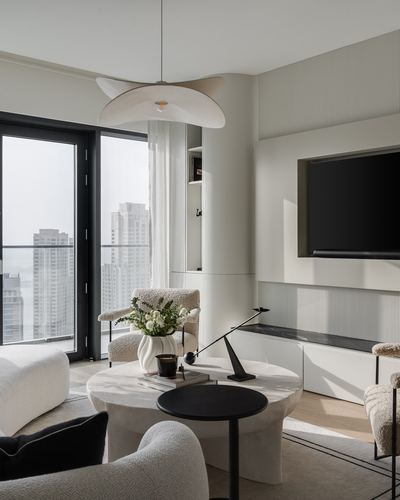 Neutral living room with boucle armchairs, round stone coffee table, and city view