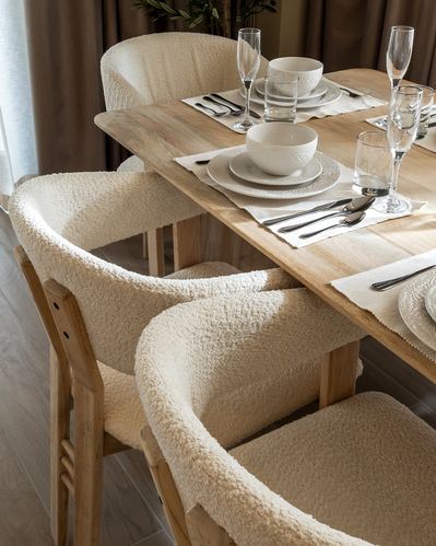 Close-up of dining table set with white plates and boucle-upholstered chairs
