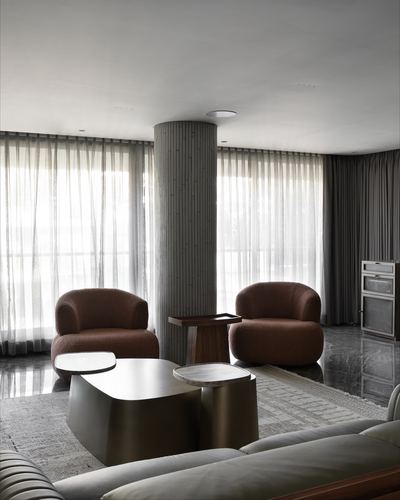 Living room with two rust boucle armchairs flanking a fluted column, sheer curtains, brass coffee tables