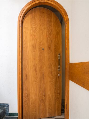 Arched wooden entrance door with brass handle set into curved plastered doorway