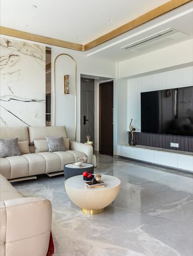 Living room with marble accent wall, gold ceiling trim, beige sofas, round marble coffee table