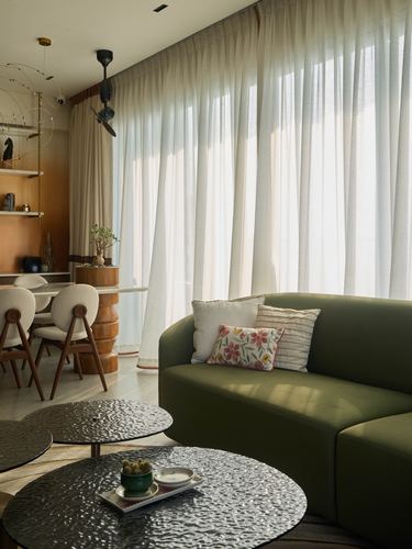 Living room with curved olive sofa, sheer curtains, and textured round coffee tables in soft daylight