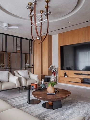 Living room with teak paneled TV wall, round wood coffee table, and statement chandelier