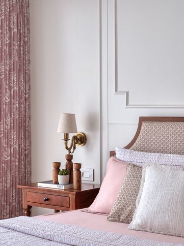Bedside vignette with wooden nightstand, brass wall sconce, and pink upholstered headboard against paneled wall