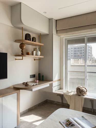 Bedroom corner with floating wood shelves, wall desk, and window seat lit by afternoon sun