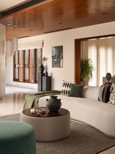 Curved beige sofa with green cushions in a living room with wood ceiling and lattice window beyond
