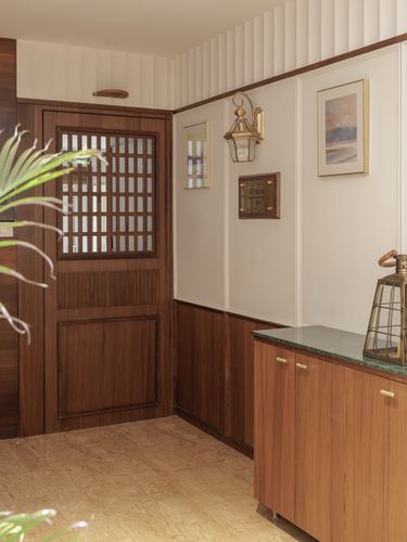 Wood-paneled entry foyer with lattice door, brass sconce, framed art, and marble-topped cabinet