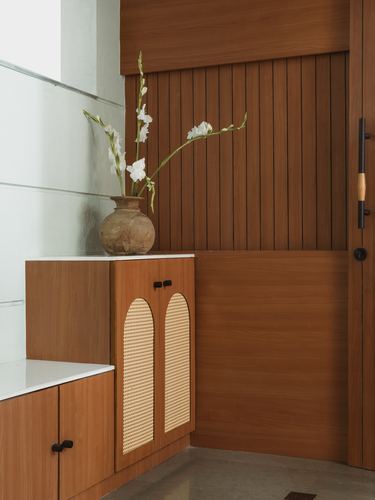 Wood-paneled foyer corner with cane-arched cabinet doors and a ceramic vase of white flowers