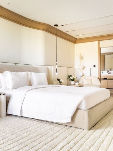 Cream minimalist bedroom with curved wood-trimmed ceiling, upholstered bed, and pendant light