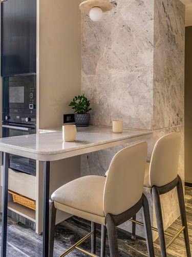 Marble-clad kitchen counter with two cream leather bar stools and pendant light