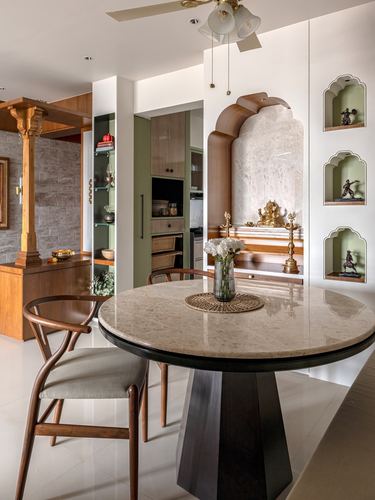 Dining table with wishbone chairs facing an arched marble pooja niche with brass idols