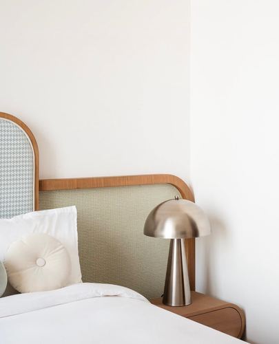 Arched wooden headboard with green woven panel beside a brushed metal mushroom lamp on nightstand