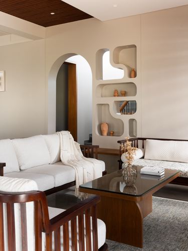 Living room with organic wall niche, arched doorway, wood-framed white sofas and glass coffee table