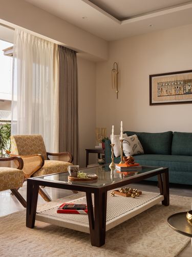 Living room with green sofa, cane armchair, wooden glass-top coffee table and sheer curtains lit by daylight
