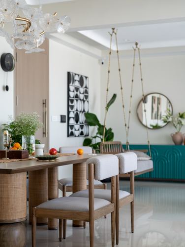 Dining table with rattan-base chairs beside a suspended wooden swing and round mirror