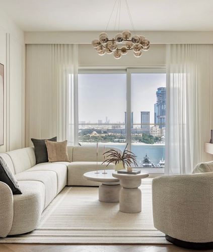 Cream boucle sectional and pedestal tables in a neutral living room with floor-to-ceiling skyline view
