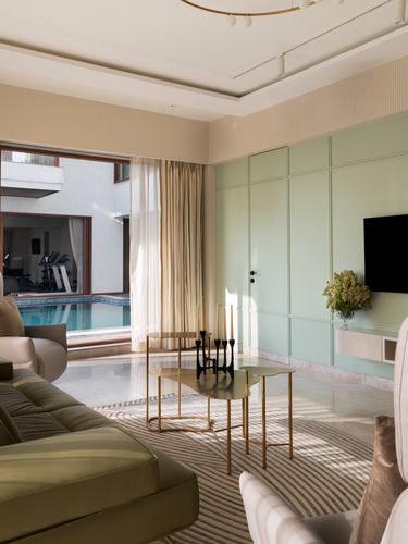 Living room with mint green paneled wall, brass tables, and a view through glass doors to a pool
