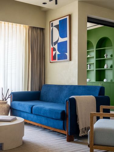 Blue velvet sofa with wooden trim before a green arched shelving niche in a living room