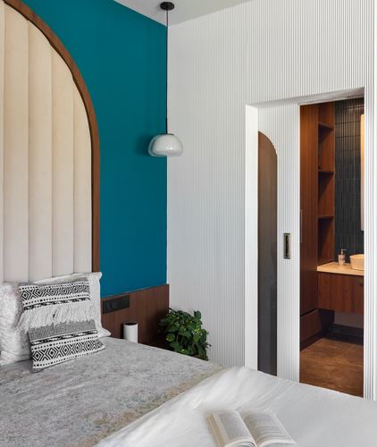 Bedroom with arched cream headboard against teal wall, fluted white wall leading to ensuite bathroom