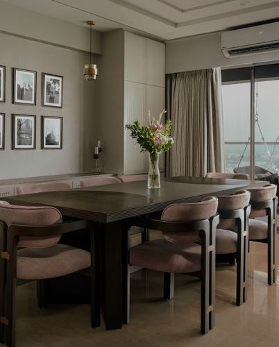 Dining room with dark wood table, pink chairs, gallery wall, and city view through glass doors