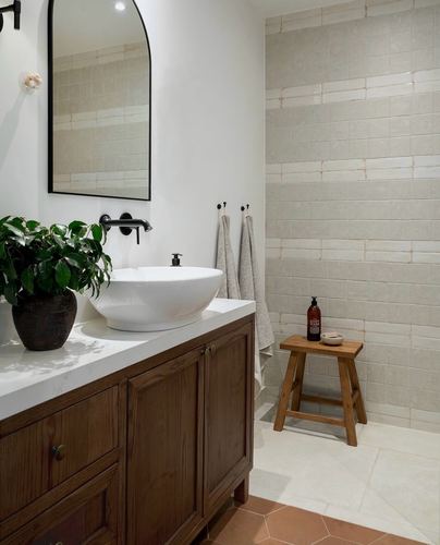 Bathroom with wooden vanity, vessel sink, arched mirror, and handmade-look tiled shower niche