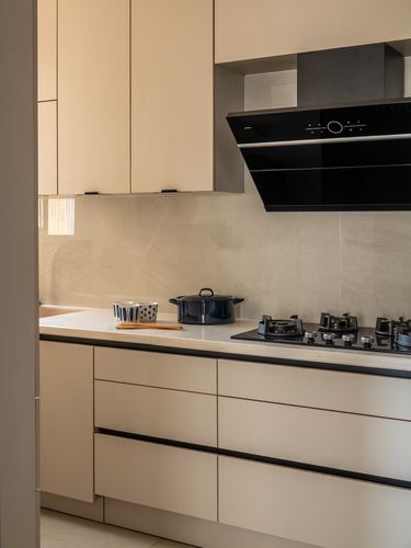 Beige kitchen counter with black gas hob, chimney hood, and black cookware against stone backsplash