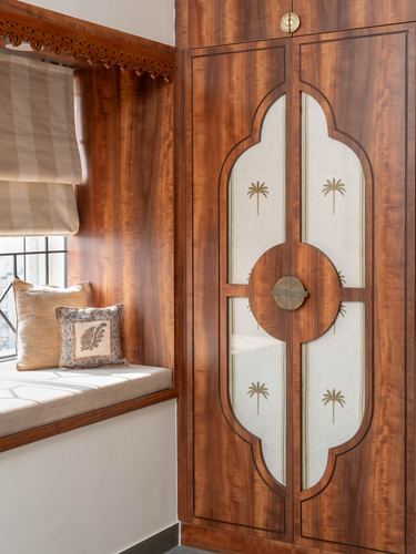 Wood-panelled wardrobe with quatrefoil inlay beside a cushioned window seat