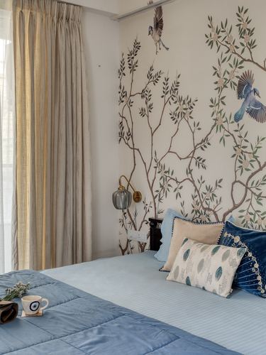 Bedroom with blue quilted bedspread against a hand-painted bird and branch mural wall