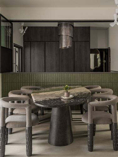 Dining table with terrazzo top and cone base surrounded by boucle chairs, green tiled wall behind