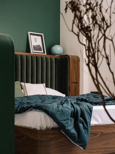 Green fluted velvet headboard with wood nightstand, teal linen bedding, and dried branch in foreground