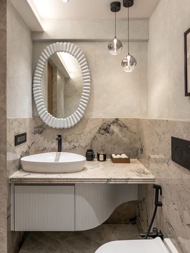 Bathroom vanity with oval scalloped mirror, vessel sink, and veined marble backsplash lit by glass pendants