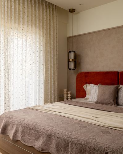 Bedroom with rust velvet curved headboard, textured taupe wall, sheer patterned curtains and hanging lantern light