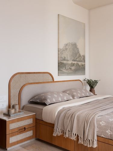 Bedroom with cane and upholstered headboard, wood nightstand, and framed landscape painting above bed
