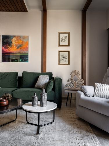 Living room with green velvet sofa, marble side table, framed art and exposed wooden beams