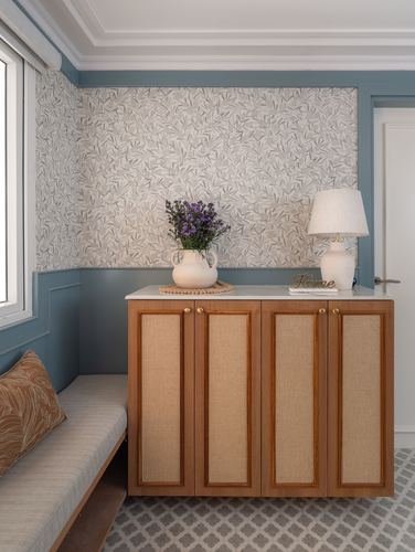 Blue-paneled foyer with wood and cane cabinet, lamp, flowers, and window seat