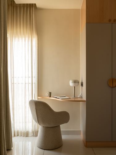 Curved boucle chair at a floating wood desk beside a sheer curtained window