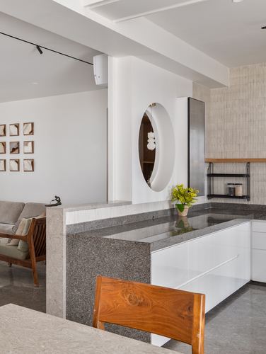Kitchen island in speckled stone with a circular niche mirror above white cabinetry