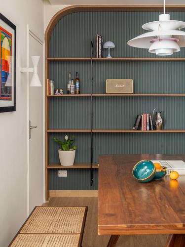 Arched wooden bookshelf with teal fluted panelling beside a walnut dining table and cane bench