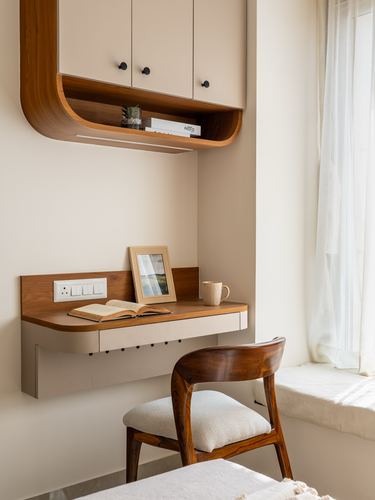 Wall-mounted wooden desk with chair beneath curved cabinet nook near window