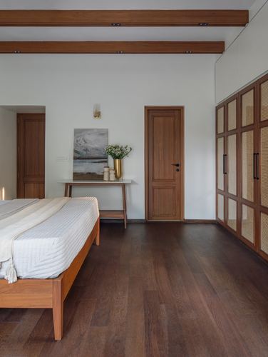 Bedroom with wooden bed, cane wardrobe, exposed beams, and dark wood flooring