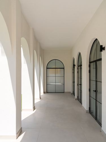 Sunlit arched colonnade corridor with black-framed arched glass doors along a plastered wall in Dubai villa