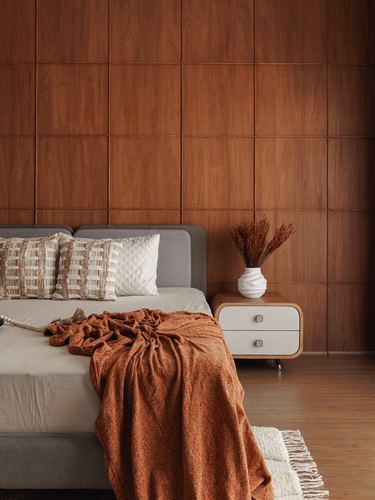 Bedroom corner with wood-panelled wall, grey upholstered bed, rust throw, and curved white nightstand