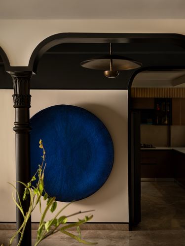 Dark arched passage with carved column and round blue wall art beside kitchen doorway
