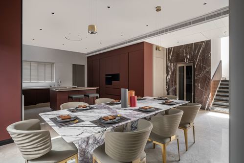 Dining table with marble top and swivel chairs before a maroon kitchen and marble-clad staircase