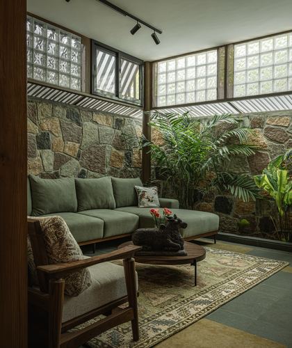 Green sofa and wooden armchair around a round coffee table against a stone wall with glass block windows