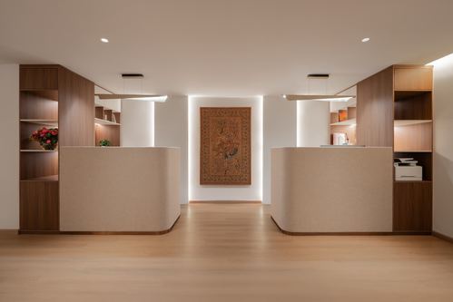 Symmetrical office reception with two curved desks flanking a lit wall tapestry and wood shelving