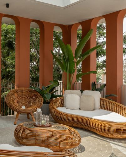 Terracotta arched balcony with rattan daybed, chair and coffee table amid potted plants